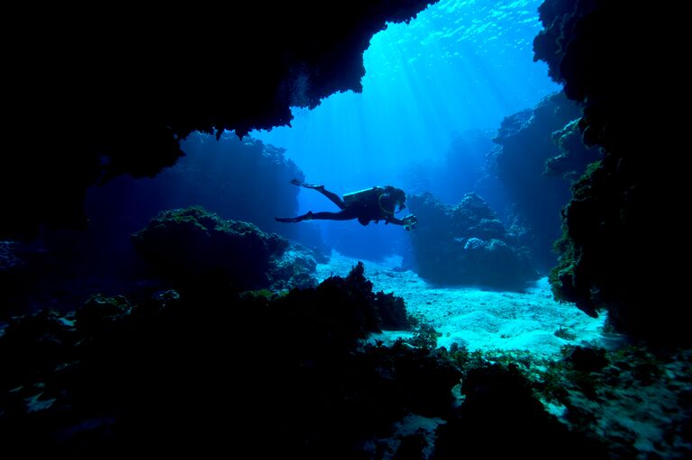 A scuba diver exploring an underwater cave in a tropical coral reef