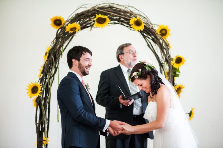 The couple exchanged vows in front of a curved branch arch decorated with bright yellow sunflowers for a pop of color in the white ceremony venue.
