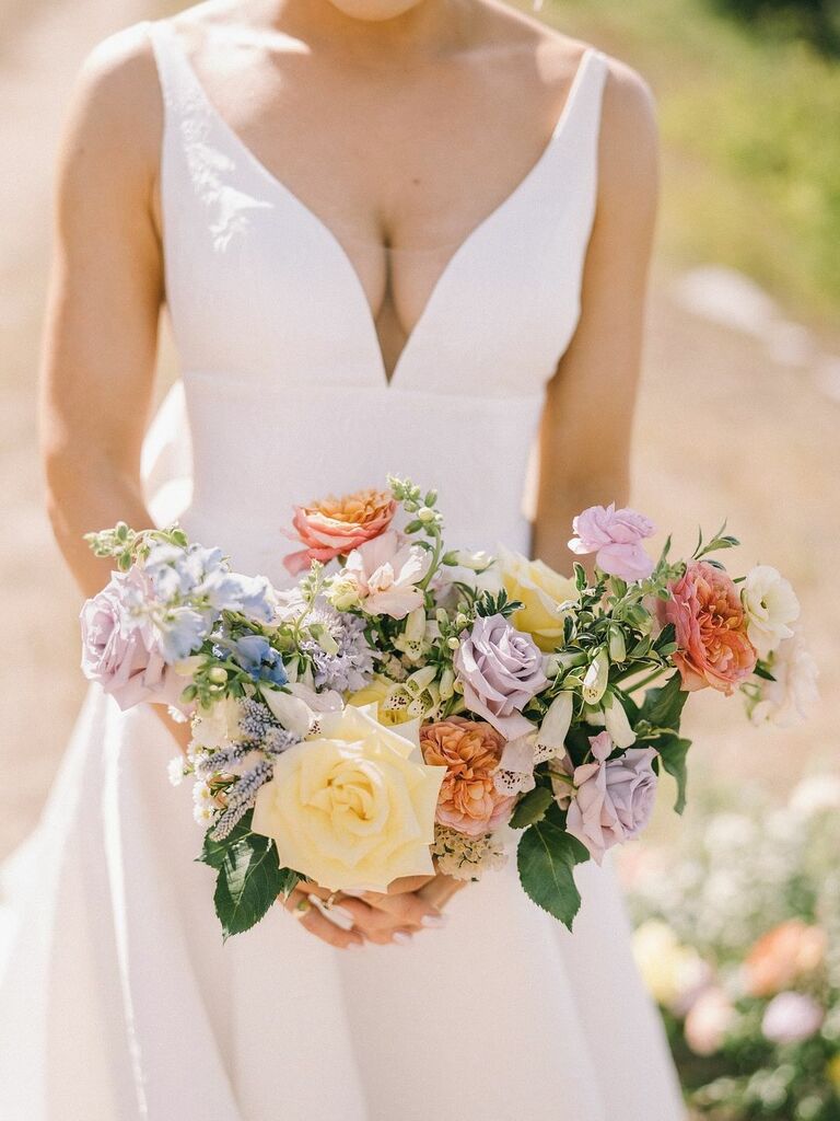 A bride carries a spring-toned bouquet in pale lavendar, yellow, peach and sky blue.