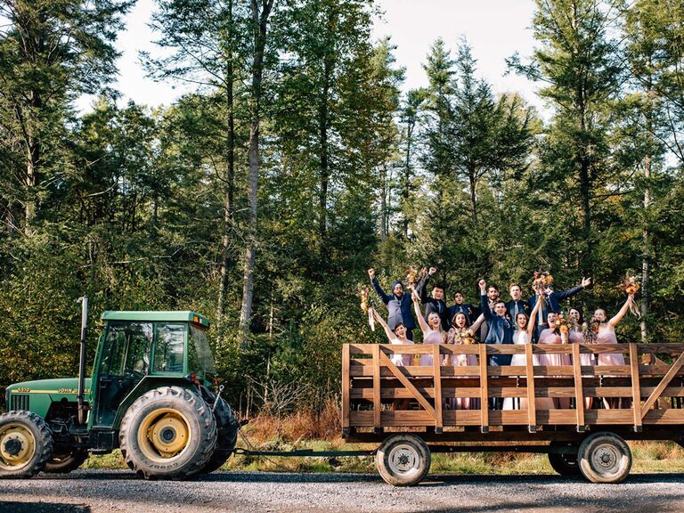 Bride and groom with bridesmaids and groomsmen on hay bale tractor at rustic barn wedding