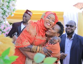 Smiling Ugandan couple embrace while loved ones look on.