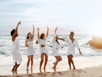 Women wearing white on beach with champagne glasses
