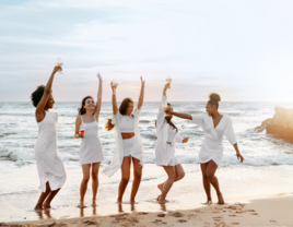 Women wearing white on beach with champagne glasses