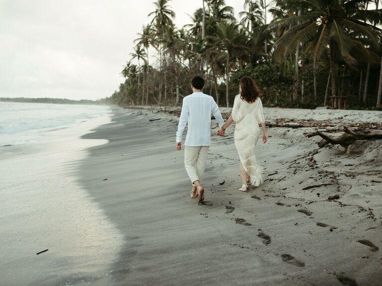 Couple walks down a beach hand in hand. 