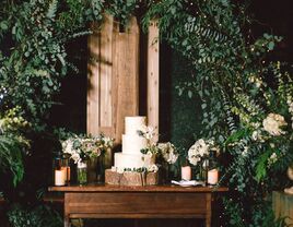 Three-tier rustic wedding cake on tree stump stand under greenery arch