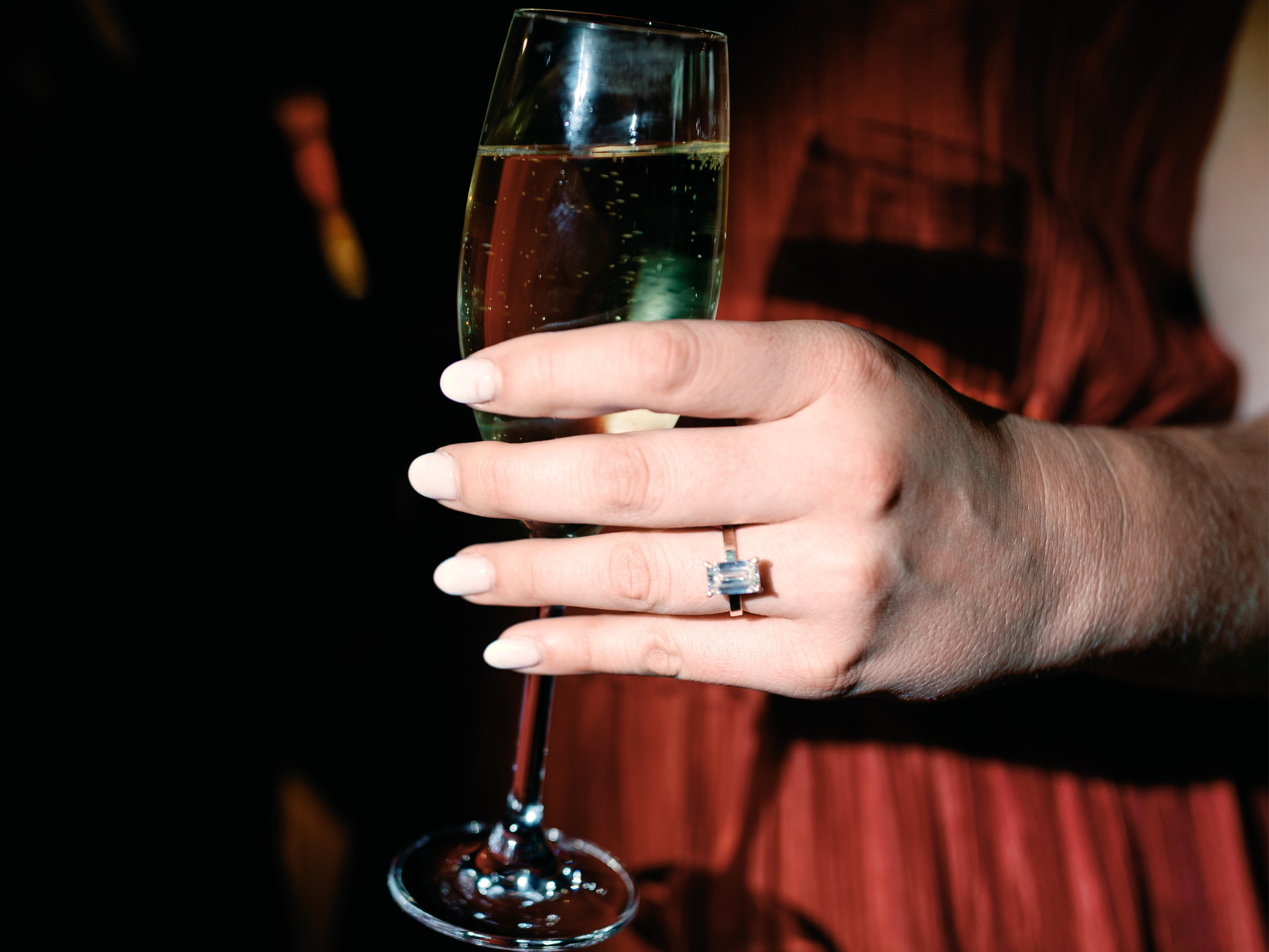 Woman holding champagne glass wearing an emerald engagement ring, The Most Popular Engagement Rings According to Our Data