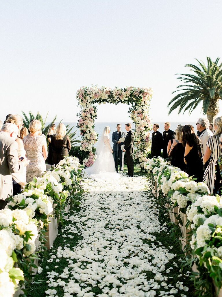 Flower-filled ceremony setup with petal-lined aisle and rose-covered arch