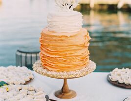 Orange and white ruffled beach wedding cake with coral topper