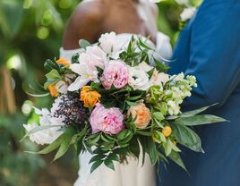 A couple stand together, holding an overflowing and vibrant peony bouquet.