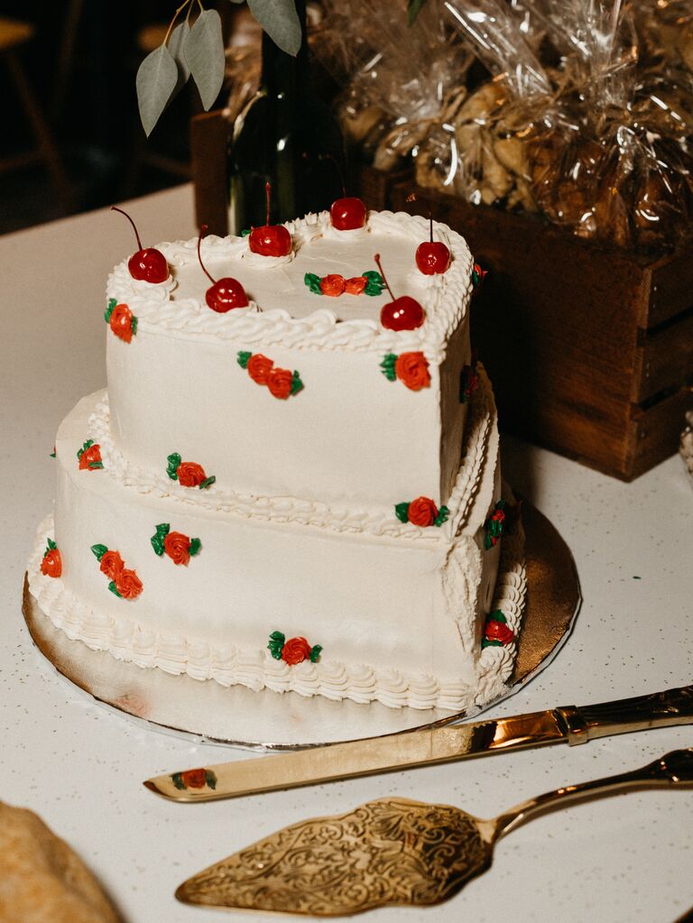 two tier heart shaped wedding cake with white frosting, red roses and cherries