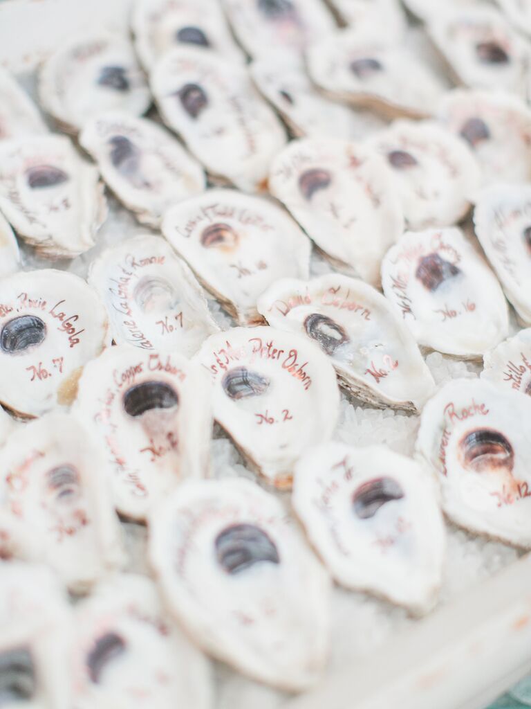 wedding escort cards made from oyster shells with guest names and table numbers written in rose gold ink