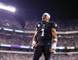 Jalen Hurts celebrates a win in a football stadium surrounded by cheering fans. 