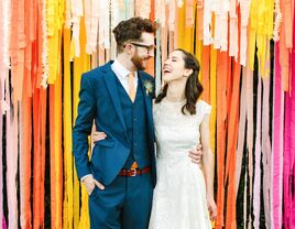Couple laughs while standing in front of colorful streamers. 