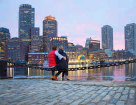 Couple sitting in front of Boston skyline at sunset