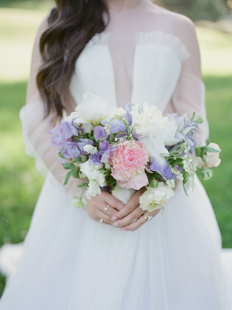 A bride holds a lavender, pink, and white peony bouquet.