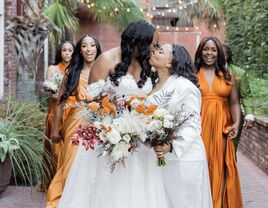 Two brides kiss while their bridesmaids cheer in the background