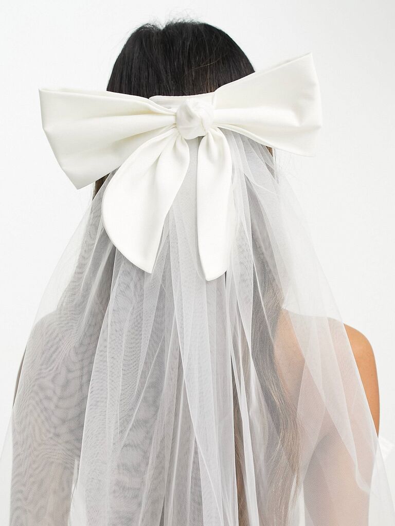 Model wears a sheer veil with a large bow attached to it. 