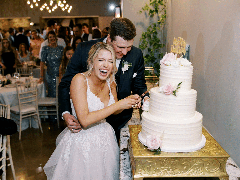 Couple laughing while cutting the wedding cake. 