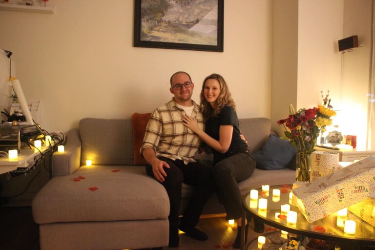 Chris proposed to Susannah on her 27th birthday! When we returned from dinner out, the apartment was beautifully decorated with rose petals, candles, and a projector showing fireworks. Chris put on the same song that had been playing when he first asked Susannah out over eight years before. Chris had Susannah sit down and read her birthday card and at the end got down on one knee and popped the question. Of course, she said yes!