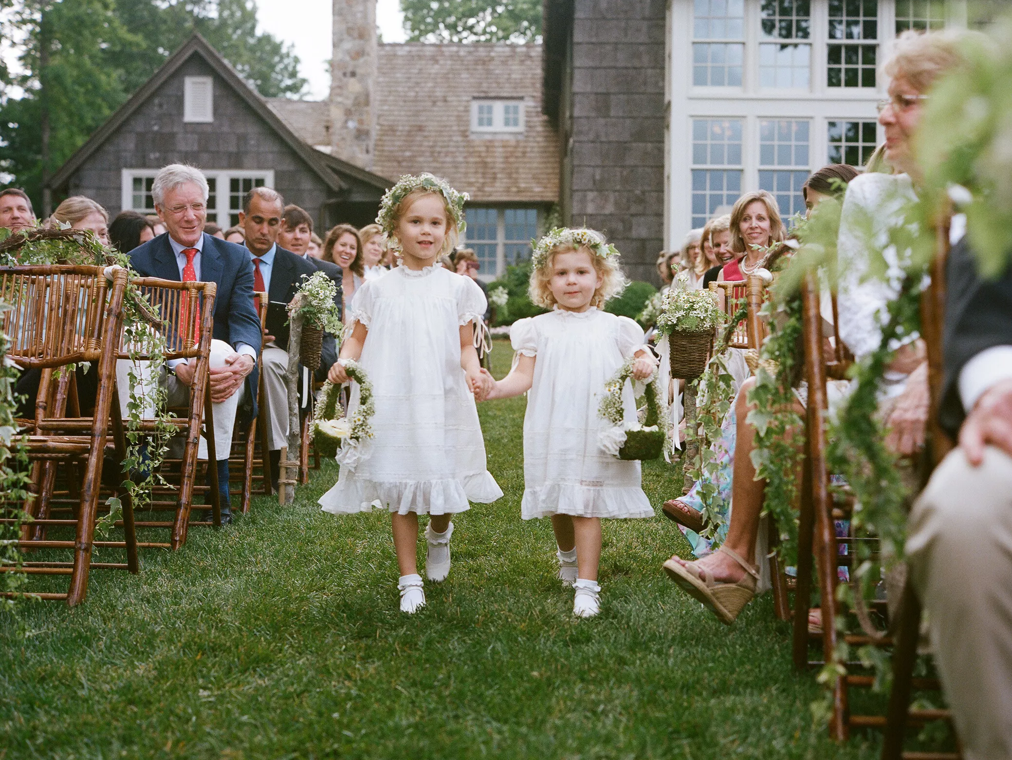 Two flower girls walk hand in hand down an aisle at this outdoor wedding.