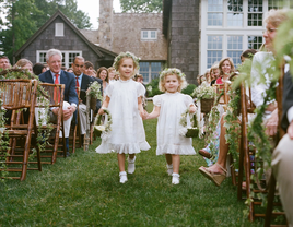 Two flower girls walk hand in hand down an aisle at this outdoor wedding.