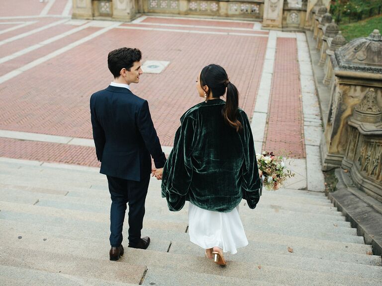 Bride wearing simple dress and green velvet coat walking down steps with groom