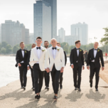 Grooms in white tuxedos and groomsmen in black tuxedos walking down sidewalk 