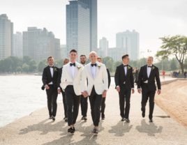 Grooms in white tuxedos and groomsmen in black tuxedos walking down sidewalk 