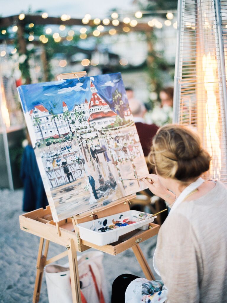 artist sits at her easel and paints outdoor wedding reception scene onto a canvas 