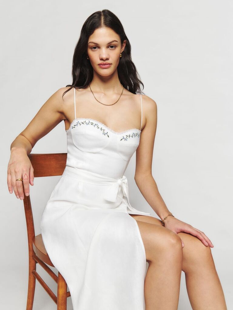 Model wears a white linen dress with floral embroidery on the bodice. 