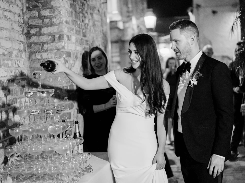 Smiling couple pouring champagne onto their elegant champagne tower. 