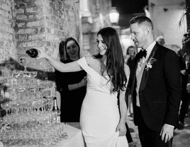 Smiling couple pouring champagne onto their elegant champagne tower. 