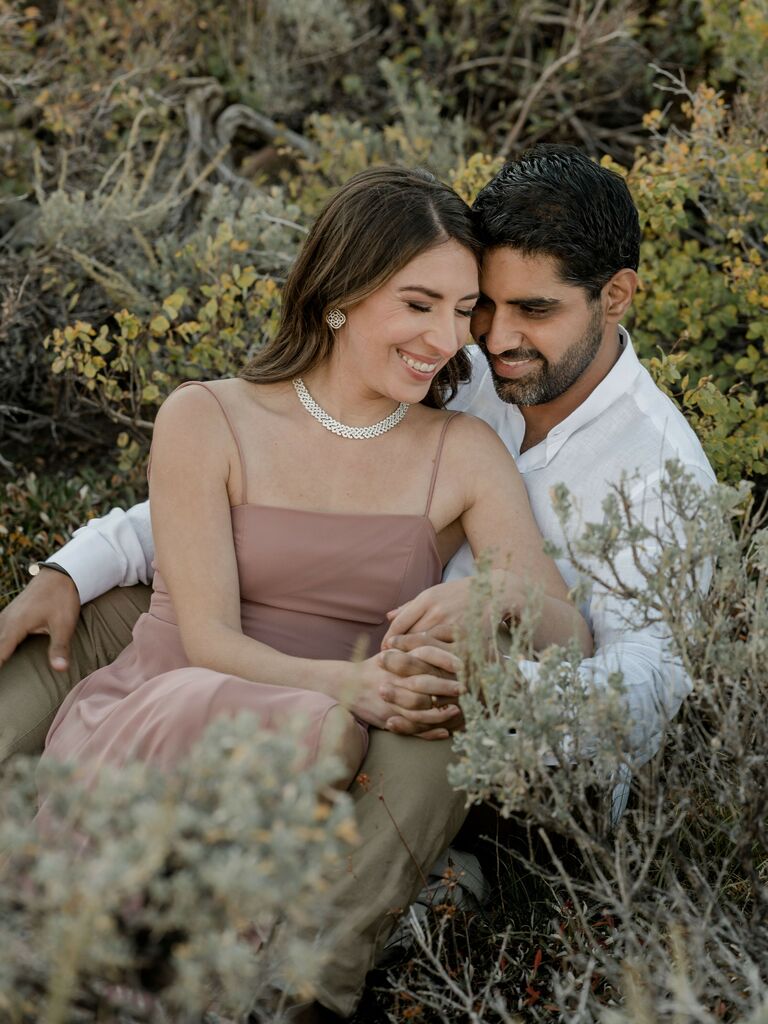 Couple smiles while sitting in a brush. 
