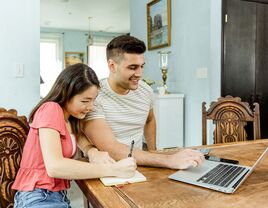 Engaged couple planning cash registry on laptop at home