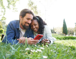 Couple laying in grass looking at phone