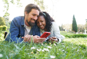 Couple laying in grass looking at phone