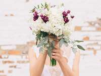 Bride holding an ivory and burgundy bouquet over her face