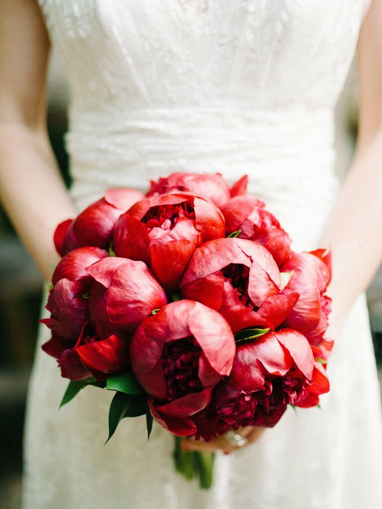 A bride holds a romantic bouquet of vibrant red peonies.