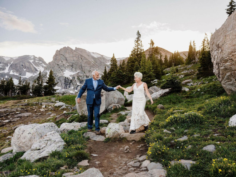Older bride and groom walking through mountain side together