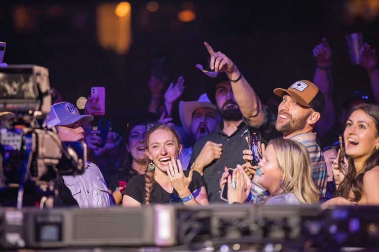 EJ gets down on one knee in the front row of the pit at the start of Luke Combs' world tour. 60,000 people witness their engagement on the big screen.