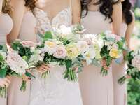 close up of bride and bridesmaids holding bouquets with pastel yellow peonies, light pink roses, queen annes lace and greenery