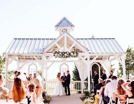 Couple exchanging their vows underneath an small outdoor shelter surrounded by loved ones