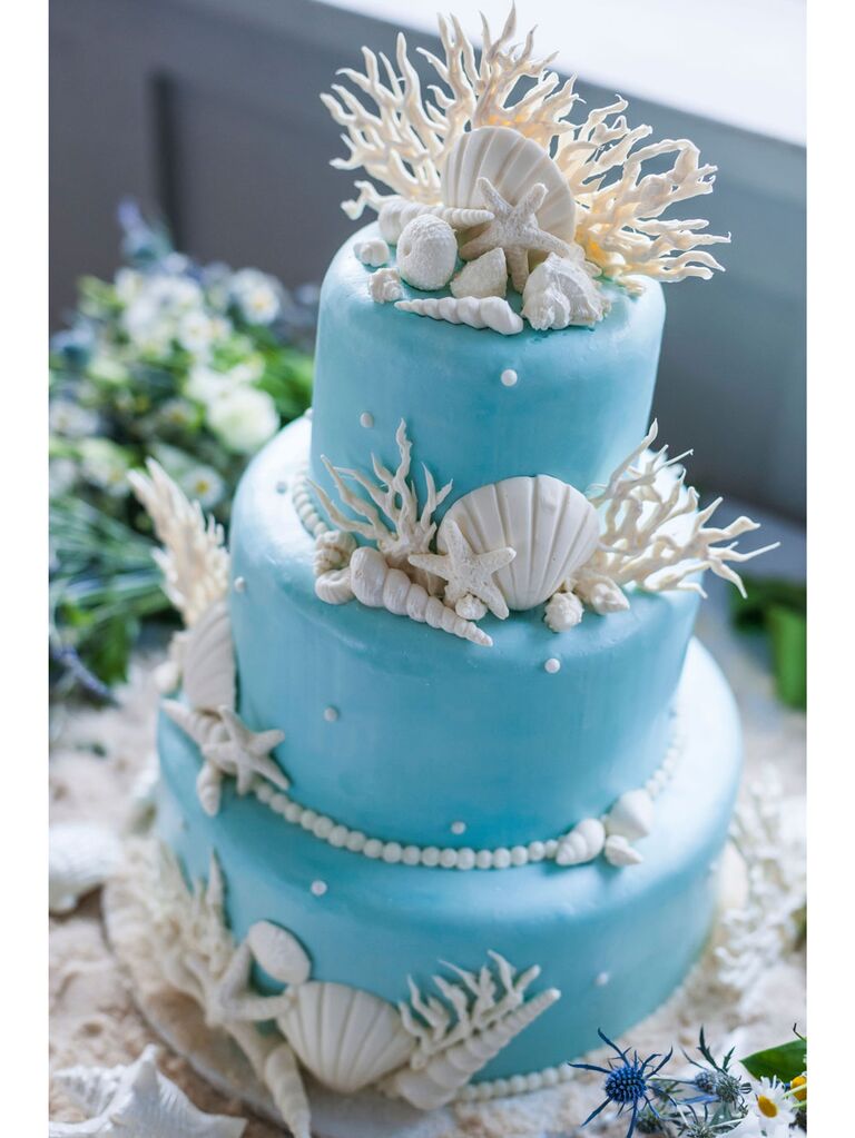 Three-tier blue beach wedding cake with white seashells and coral decor