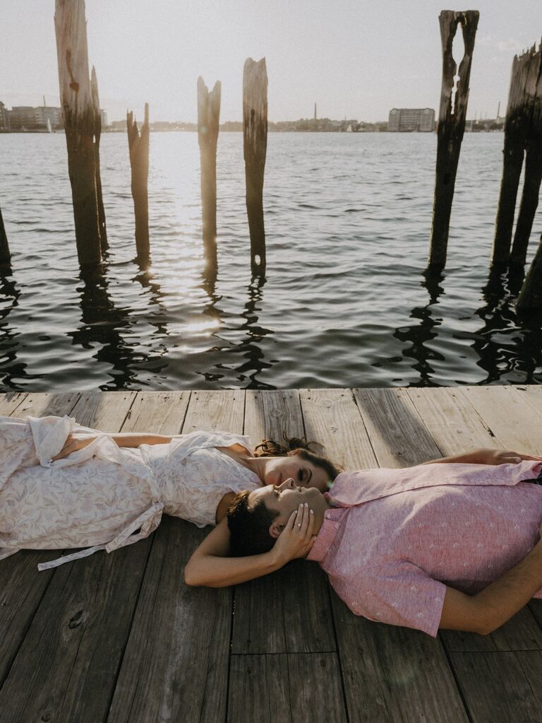 Couple pose on a boardwalk for their summer engagement photo session. 
