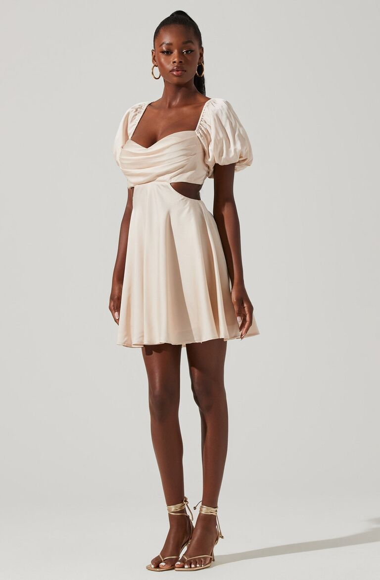 Model wears a champagne-colored mini dress with puffed sleeves. 