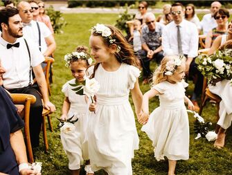 three flower girls wearing ivory dresses walking down the aisle at a wedding ceremony