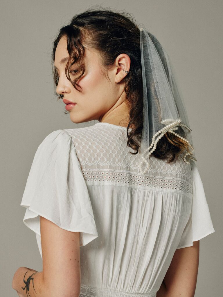 Model wears a chic short veil with pearls stitched on the hem. 