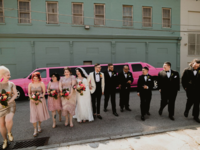 Wedding party walking in front of pink limo with bride and groom
