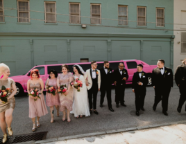 Wedding party walking in front of pink limo with bride and groom