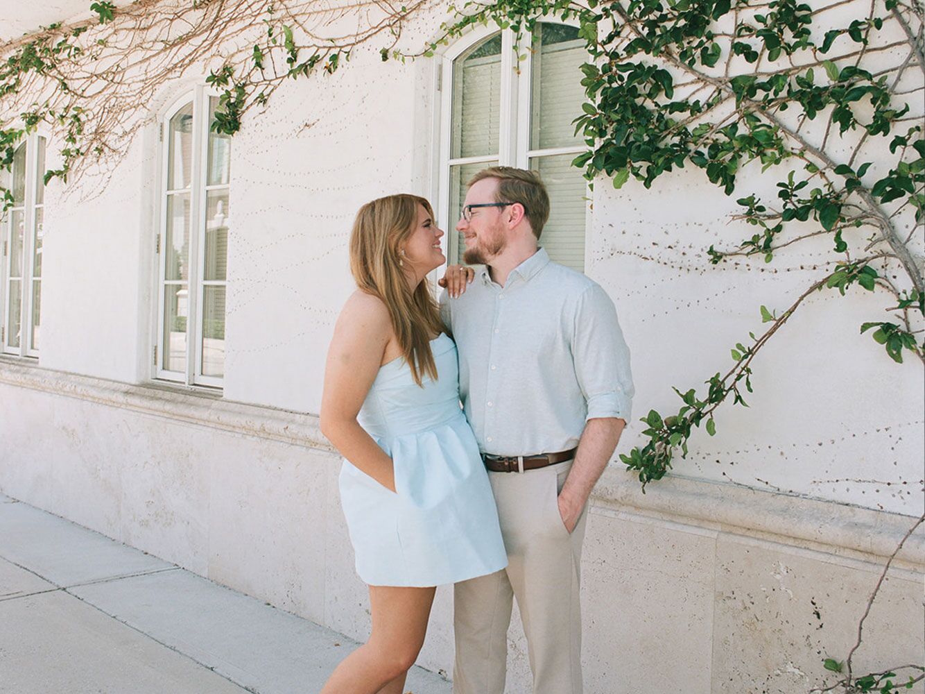 Couple standing outside of building posing and smiling at eachother